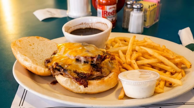Cheeseburger with melted cheddar, fries, and a side of au jus on a white plate.
