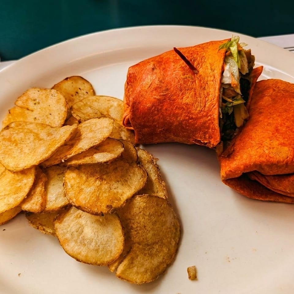 A red tortilla wrap with lettuce and meat, served with a side of potato chips.