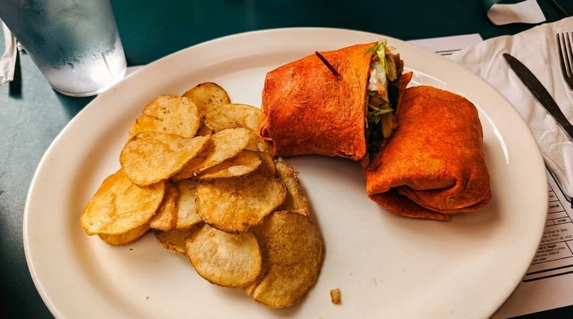 A red tortilla wrap with lettuce and meat, served with a side of potato chips.
