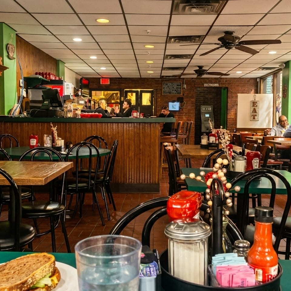 Cozy diner interior with wooden paneling, green walls, patrons dining, and a sandwich on a table.